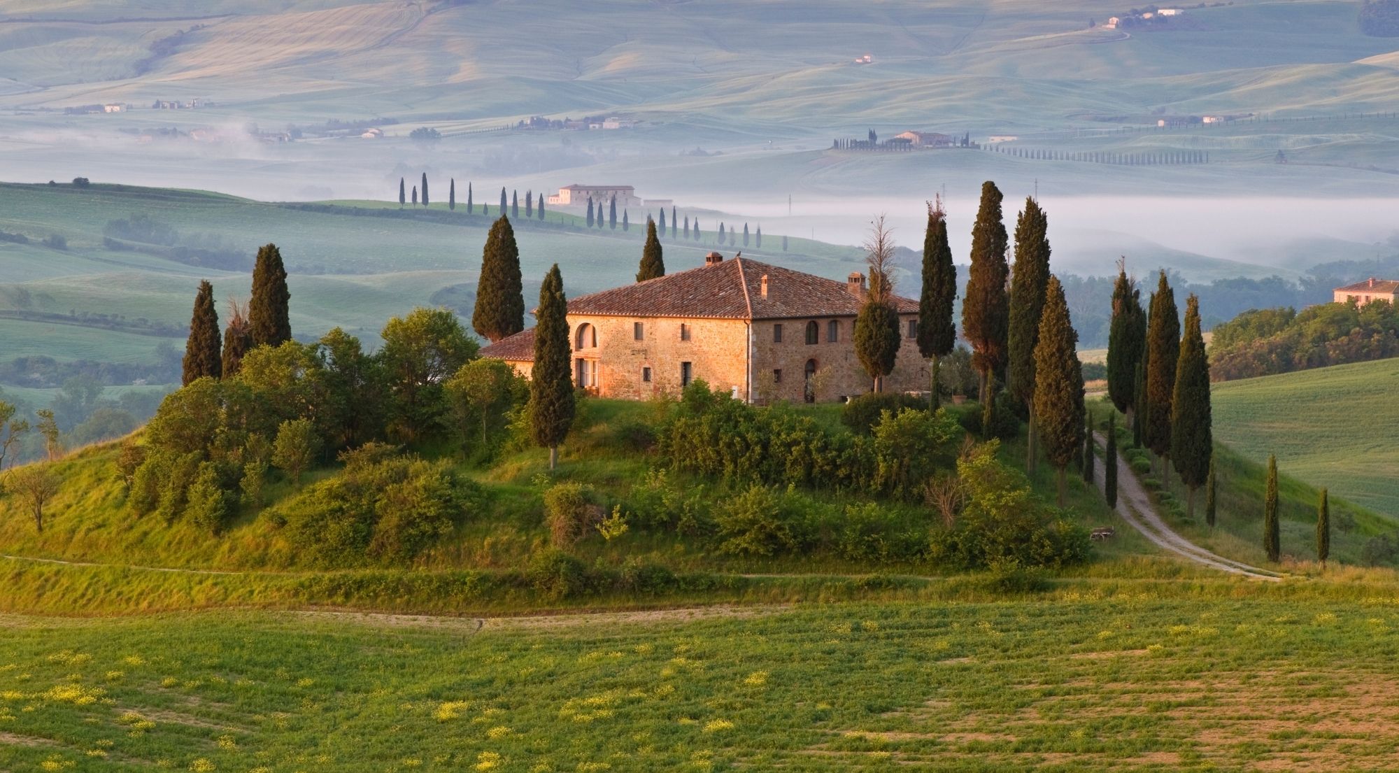 A classic Tuscan stone farmhouse ringed by cypress trees in the misty Chianti valley